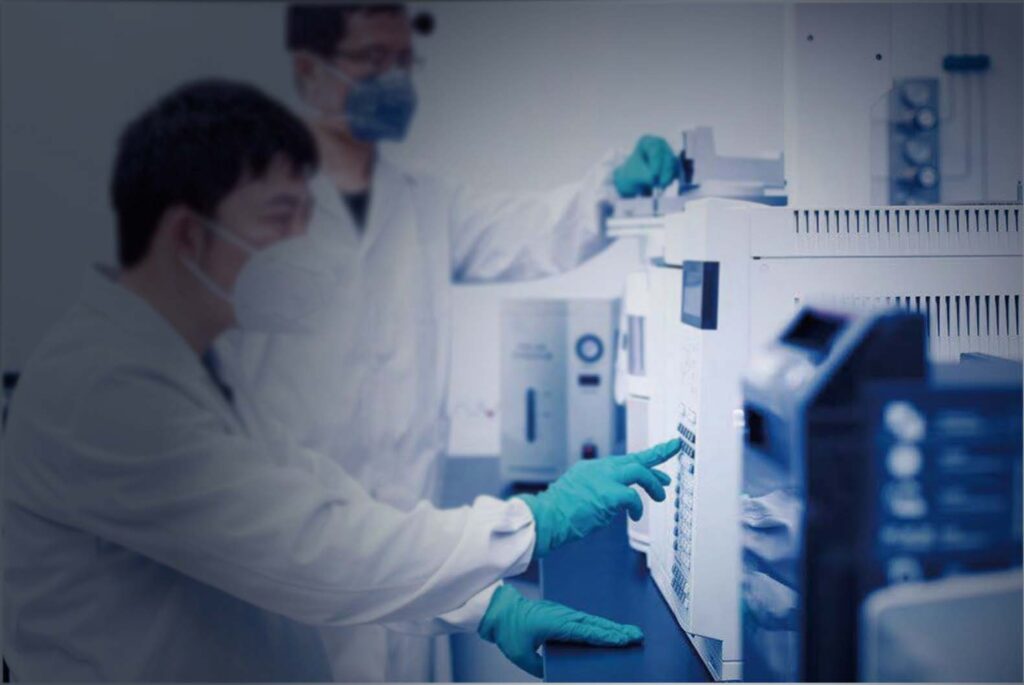 Two technicians wearing lab coats, rubber gloves, and face masks working in a laboratory